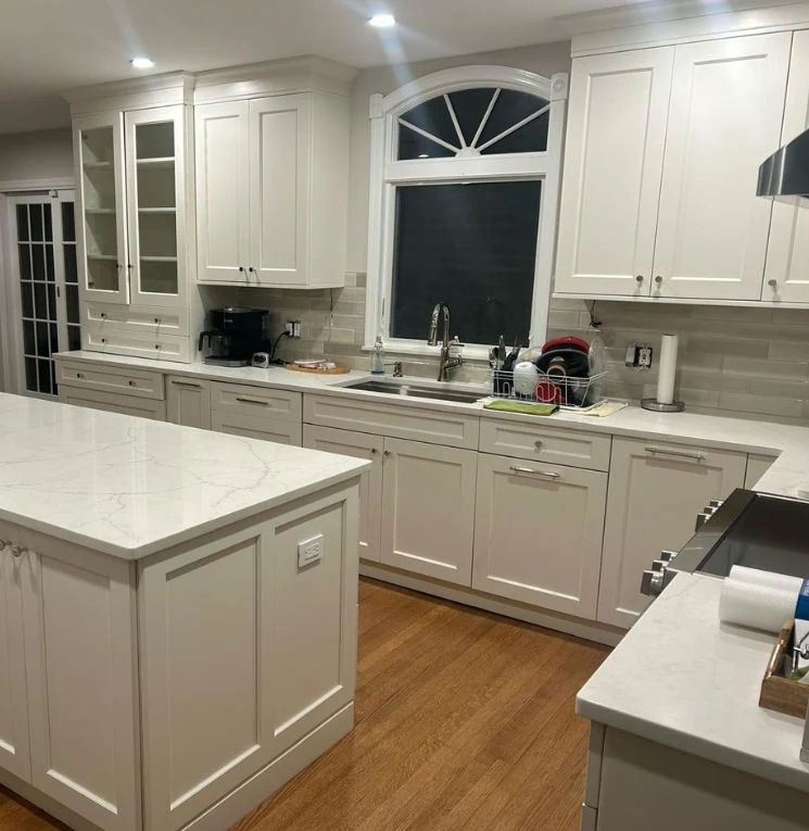 White kitchen cabinetry around an arched window with a sink and island